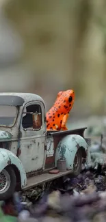 Miniature vintage truck with orange frog in forest setting.