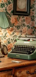 Vintage green typewriter on wooden desk with floral wallpaper.