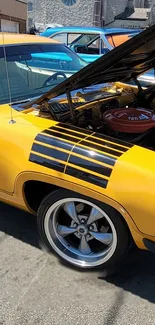 Vintage yellow muscle car with open hood showing engine.