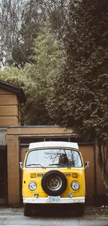 Vintage yellow van parked by brown house with greenery.