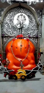 Bright orange Ganesh idol in temple alcove with ornate decor.