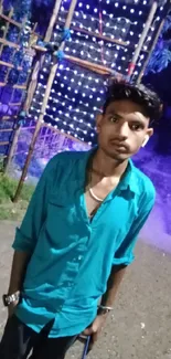 Young man in teal shirt at night event with colorful lights.