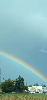 A vibrant rainbow arches over a serene countryside landscape under a blue sky.