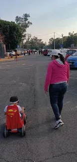 Child in superhero cape on scooter with adult in park setting.