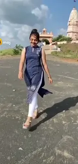 Woman walking on a path near a temple with a blue sky.