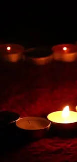 A row of flickering candles on a dark red background creates a warm ambiance.