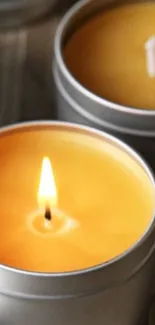 Close-up of a lit candle in a silver tin, emanating a warm amber glow.