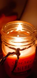 Warm candle in a glass jar radiating a soft glow against a dark backdrop.