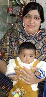 Mother holding baby in colorful attire, warm family scene.