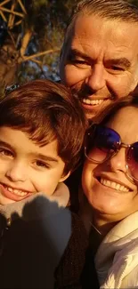 A family smiles brightly under warm sunlight outdoors.