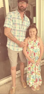 Father and daughter in sepia-tone summer attire posing by a glass door.