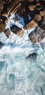 Top-down view of ocean waves crashing over rugged rocks, creating a serene wallpaper.