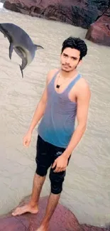 A man standing by a waterfall with a dolphin jumping in the background.