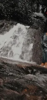 Person standing by waterfall with lush background.