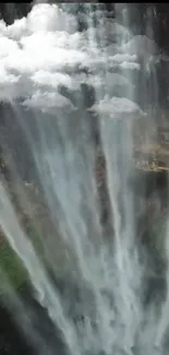 Majestic waterfall with mist and clouds over lush green landscape.