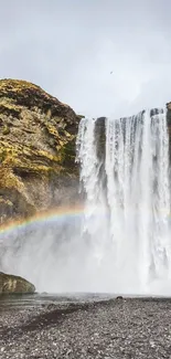 Majestic waterfall with rainbow and misty surroundings.