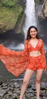 Woman in orange outfit by a scenic waterfall.