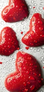 Four red heart-shaped objects with water droplets on a surface.