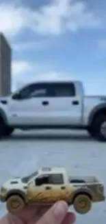 Real truck and toy model under a blue sky and gray building.