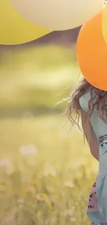 Girl holding yellow and orange balloons in a sunny field.