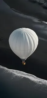 White hot air balloon soaring above a dark beach.