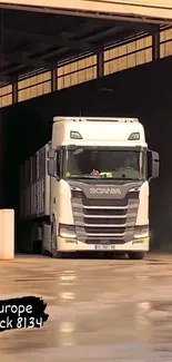 White Scania truck exiting a warehouse, beige tones.