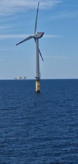 A wind turbine stands in the ocean against a clear blue sky, capturing renewable energy.