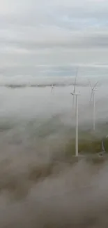 Misty fields with wind turbines emerging through fog, creating a serene landscape.