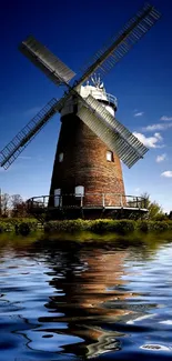 Windmill reflecting on blue water under a clear sky.