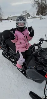 Child in pink jacket riding snowmobile in snowy landscape.