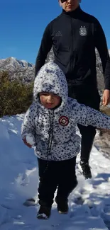 Child in snow with mountains and blue sky background.