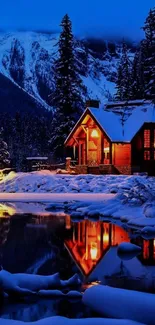 Warmly lit cabin amidst snowy landscape with lake reflection.