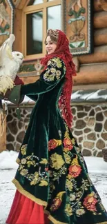 Woman in traditional dress holding an owl by a snowy log cabin.