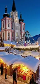 Snowy winter market by illuminated cathedral at dusk.