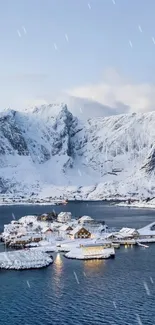 Snowy village by lake with towering mountains.