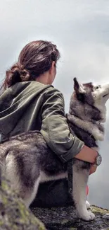 Woman embraced with Husky on mountain top under a cloudy sky.