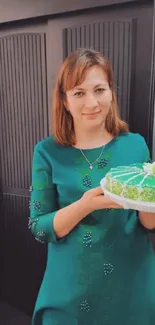 Woman in green dress holding a decorated cake.