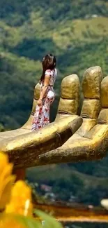 Woman stands on giant golden hand with scenic background.