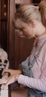 Woman in overalls plays piano with a cat nearby.