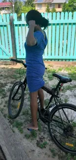 Woman with bicycle near turquoise fence.