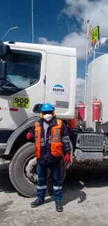 Worker in safety gear stands beside a transport truck on a clear day.