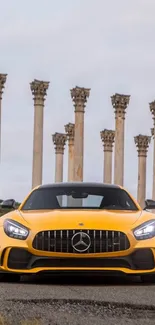 Yellow sports car in front of historic stone pillars.