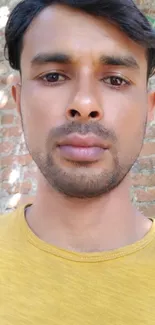 Person wearing yellow shirt in front of a rustic brick wall.