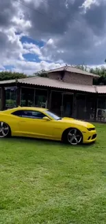 Yellow car on grass with house and cloudy sky background.