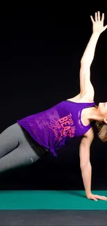 A woman doing a side plank yoga pose on a green mat against a black background.