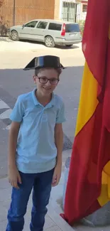 Young boy with hat, next to red and yellow flag.