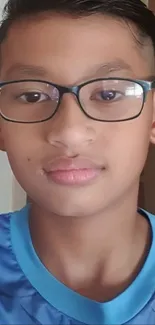 Young boy with glasses in blue shirt, looking ahead.