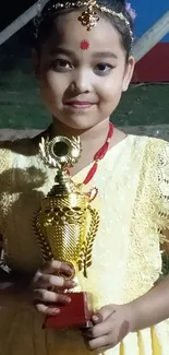 Little girl in yellow dress holding a trophy.