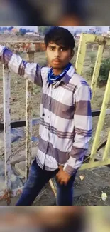 Young man in plaid shirt by a rustic fence.