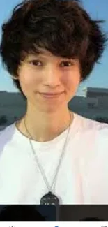 Young person with stylish hair and a necklace against a blue sky.